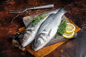Raw Sea Bass, Branzino fish with thyme and lemon. Dark background. Top view photo