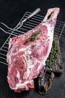Marinated raw lamb mutton Leg Thigh with thyme and spices. Black background. Top view photo