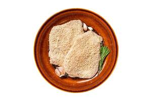 Raw Breaded German Wiener schnitzel on a rustic plate with herbs. Isolated, white background. Top view. photo