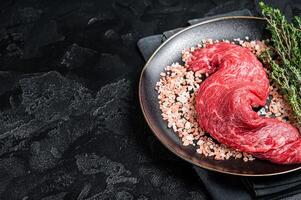 Raw Machete beef meat steak or hanging tender cut on plate with sea salt and thyme. Black background. Top view. Copy space photo