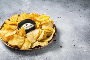 Variety of Potato chips in a plate served with dip sauce. Gray background. Top view. Copy space photo