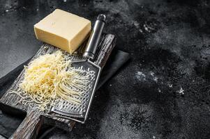Grated cheese for cooking on a cutting board . Black background. Top view. copy space photo