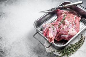 Marinated mutton lamb whole shoulder, raw meat in a steel tray with herbs and spices. White background. Top view. Copy space photo