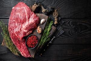 Tri Tip black angus beef steak on cutting board with herbs, raw meat. Black Wooden background. Top view. Copy space photo
