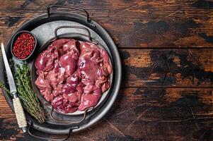 Fresh Raw chicken liver, poultry giblets in steel tray with herbs. Wooden background. Top view. Copy space photo