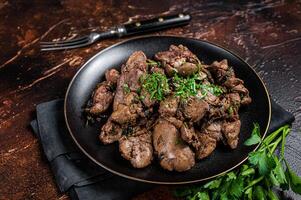Fried chicken liver with onions and parsley in a plate. Dark background. Top view photo