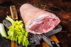 Fresh Raw pork shank knuckle on a butcher board with herbs for cooking. Dark background. Top view photo