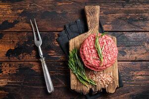 Raw minced homemade farmers grill beef burgers on chopping board with salt and rosemary. Wooden background. Top view photo