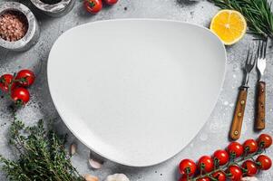 Food cooking and healthy eating background with empty rustic plate and fresh seasoning, knife, fork and vegetables ingredients. Gray background. Top view. Copy space photo