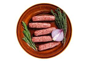 Raw kofta meat kebabs sausages on a plate with herbs. Isolated on white background. photo