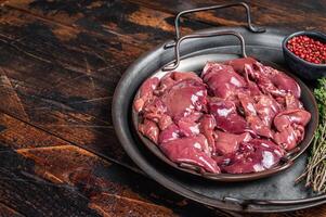 Fresh Raw chicken liver, poultry giblets in steel tray with herbs. Wooden background. Top view. Copy space photo