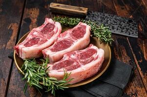 Uncooked Raw lamb loin chops steaks, saddle in plate with rosemary and thyme. Wooden background. Top view photo