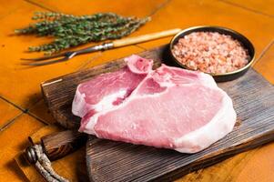 Fresh Raw pork t-bone chop meat steak on cutting board. Orange background. Top view photo