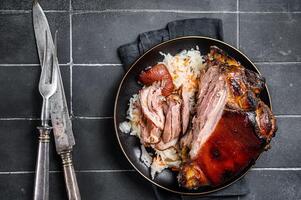 Roast Pork Ham Hock, knuckle with Sauerkraut on a plate. Black background. Top view photo