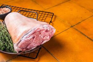 Raw pork shank knuckle in a steel tray with herbs. Orange background. Top view. Copy space photo