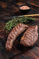 Grilled Sirloin flap or Bavette beef meat steak on a griil with herbs. Wooden background. Top view photo