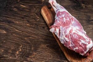 Mutton meat. Raw whole lamb leg thigh on butcher board. Wooden background. Top view. Copy space photo