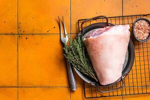 Raw pork shank knuckle in a steel tray with herbs. Orange background. Top view. Copy space photo