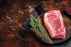 Uncooked Raw striploin or club steak on wooden board with thyme. Dark background. Top view. Copy space photo