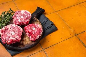 Raw lamb neck chops, fresh mutton meat on a butcher board with herbs. Orange background. Top view. Copy space photo