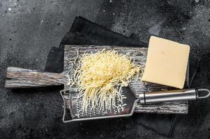 Grated cheese for cooking on a cutting board . Black background. Top view photo