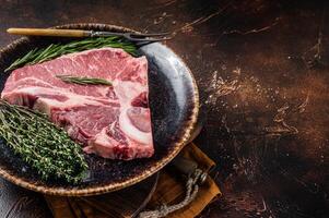 Dry aged Raw porterhouse beef meat Steak, fresh T bone on rustic plate with spices. Dark background. Top view. Copy space photo