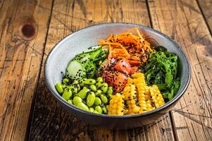 Poke bowl with fresh Salmon fish, rice, seaweed, edamame, cucumber and black sesame. Wooden background. Top view photo