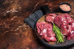 Sliced Raw chicken liver, fresh fowl offals on wooden board. Dark background. Top view. Copy space photo