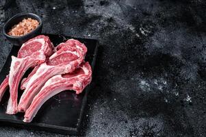 Uncooked lamb mutton chops, raw meat steaks. Black background. Top view. Copy space photo