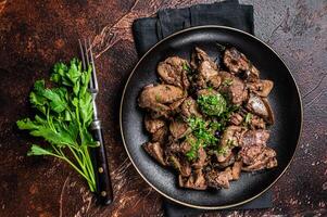 Fried chicken liver with onions and parsley in a plate. Dark background. Top view photo