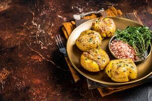 Crushed, smashed potatoes baked with rosemary and thyme on plate. Dark background. Top view. Copy space photo
