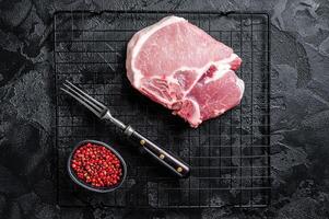 Uncooked Raw pork T bone chop meat steak on grill. Black background. Top view photo