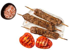 Roasted Turkish Adana shish kebab on a board with grilled tomato. Isolated on white background, top view. photo