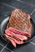 Grilled Flap or Flank Steak, sliced on a plate. Black background. Top view photo