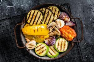 Grilled vegetables, bell pepper, zucchini, eggplant, onion and tomato. Black background. Top view photo