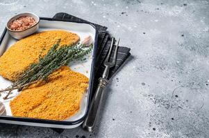 Cooking raw chicken schnitzel in breadcrumbs, uncooked meat steak. Gray background. Top view. Copy space photo