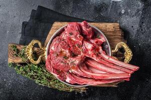 Lamb mutton chop steak, raw meat cutlet in a skillet with herbs. Black background. Top view photo