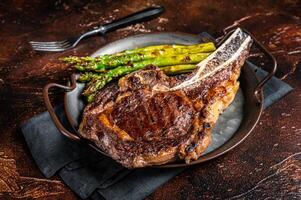 BBQ Grilled Tomahawk or Cowboy with bone beef steak, roasted asparagus. Wooden background. Top view photo