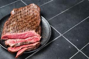 Grilled Flap or Flank Steak, sliced on a plate. Black background. Top view. Copy space photo