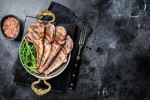 Grilled Lamb mutton Chops steaks in a skillet with green salad. Black background. Top view. Copy space photo