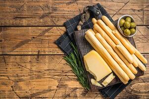 Traditional italian appetizer grissini bread sticks on wooden board with olives and parmesan cheese. Wooden bakground. Top view. Copy space photo
