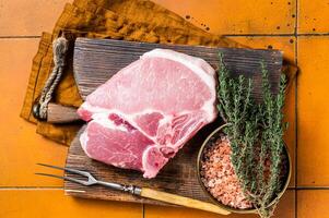 Fresh Raw pork t-bone chop meat steak on cutting board. Orange background. Top view photo