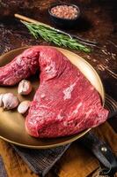 Raw tri-tip triangle roast or bottom sirloin steak on plate with herbs. Dark background. Top view photo