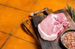 Fresh Raw pork t-bone chop meat steak on cutting board. Orange background. Top view. Copy space photo