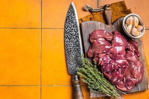 Raw chicken liver, fresh fowl giblets on wooden board. Orange background. Top view. Copy space photo