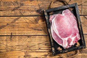 Raw pork cutlet or chop steaks in a wooden tray. Wooden background. Top view. Copy space photo