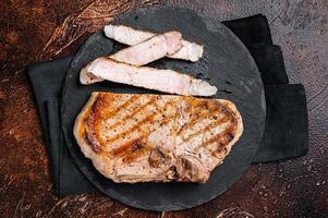 Roast BBQ pork Chop or T-bone meat steak sliced on a board. Dark background. Top view photo