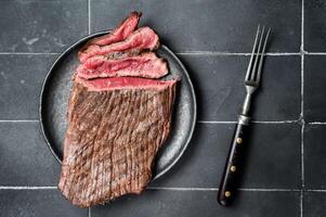 Grilled Flap or Flank Steak, sliced on a plate. Black background. Top view photo
