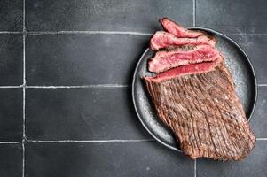 Grilled Flap or Flank Steak, sliced on a plate. Black background. Top view. Copy space photo