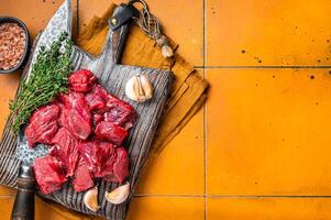 Raw beef meat chopped in cubes on wooden cutting board for cooking stew. Orange background. Top view. Copy space photo